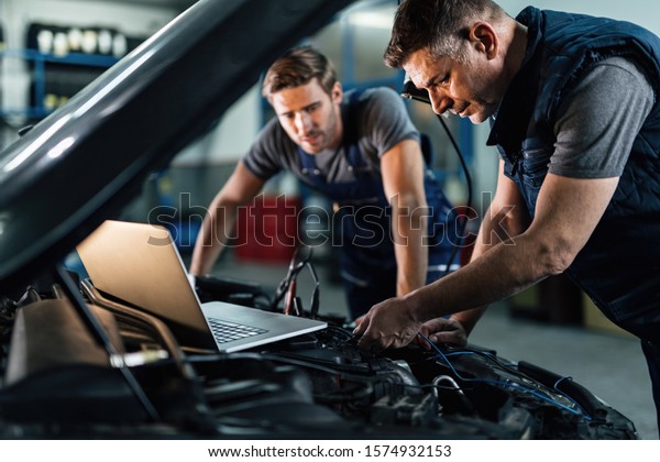 Car repairmen using laptop while doing car\
engine diagnostic in auto repair shop.\
