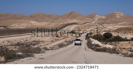 A car in restricted military zone along the border between Israel and Egypt along patrol road 10 in remote part of the Negev desert and the Sinai desert. The border barbed wire fence along the road 10