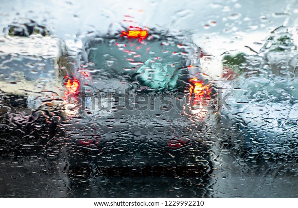 The car in a reverse gear\
braking and paying attention when parking to prevent an accident in\
a bad rainy weather viewed through a wet windscreen with blur\
effect.