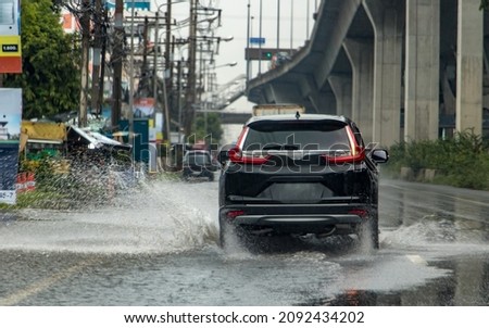 The car ride through a puddle from which water is sprayed. Traffic in the rain season, Bangkok, Thailand.