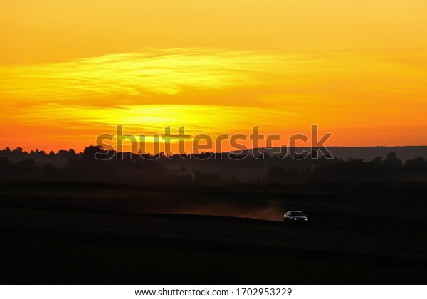 The car rides across the field during\
sunset, dust from the car, selective\
focus