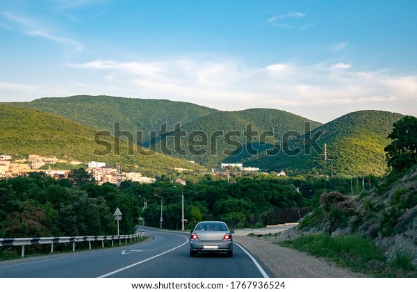 Car rides along the\
highway among green mountains in sunny weather. Car rides on a road\
through forest hills.
