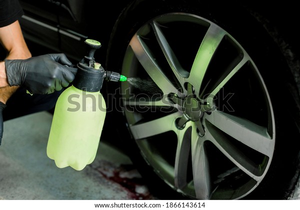 Car rims\
cleaning, car detailing wash concept. Cropped close up photo of\
male hand in black rubber glove with sprayer bottle, washing car\
alloy wheel at car wash and detailing\
service