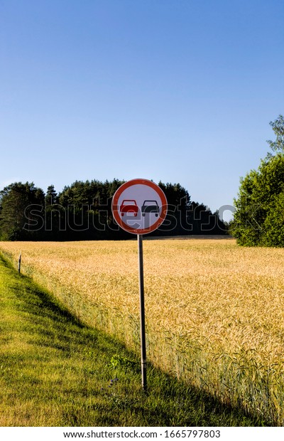 car road sign prohibiting\
overtaking on the road, on the background of the sky and the\
field