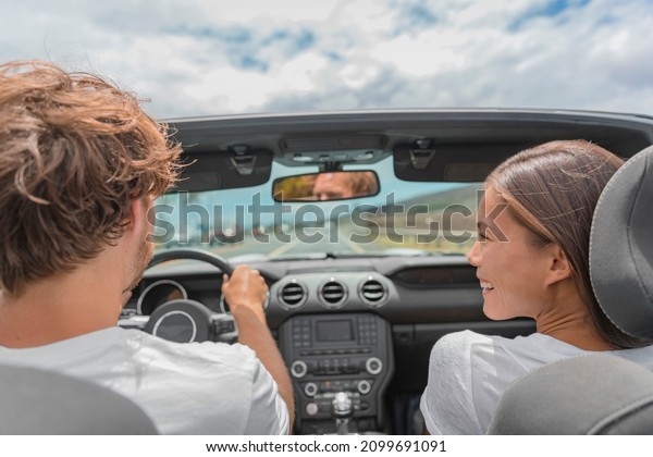 Car road trip man driving convertible sports\
car, Asian woman girlfriend looking smiling at him. Summer travel\
vacation.