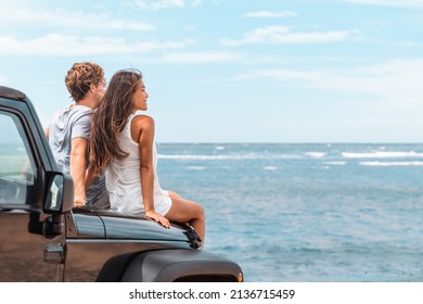 Car road trip travel couple tourists enjoying ocean view relaxing on hood of sports utility car. Happy Asian woman, man friends smiling on beach.
