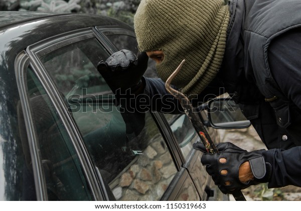 Car robbery in\
mask looking inside car\
window