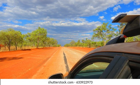 Car with roof rack driving through the Red Center in the Outback of Australia on a long straight road with blue cloud pattern sky 