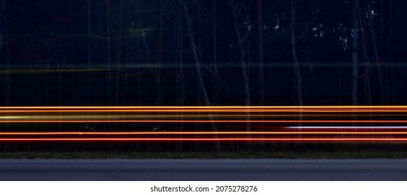 Car Running Lights In Blurred Motion On Highway Against Dark Blurred Forest Background