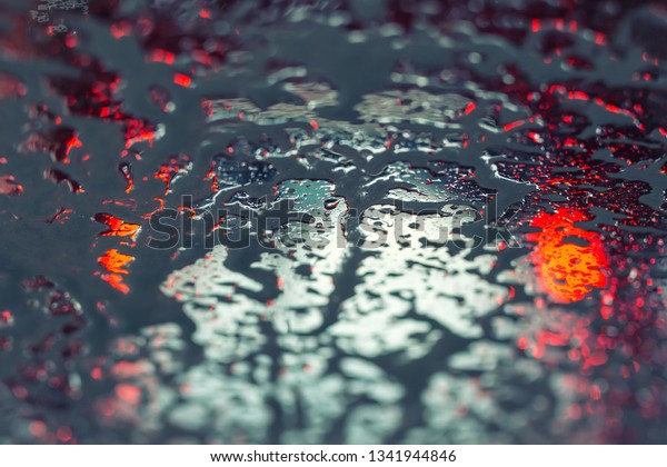 Car running through automatic carwash.\
Windscreen view from inside. Abstract wet windshield background.\
Red brake lights of car ahead. Washing\
conveyor