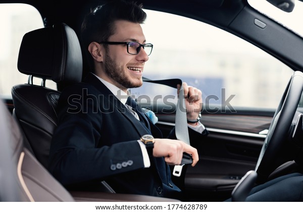Car Safety. Happy\
bearded business man in glasses fastening seat belt in auto,\
driving to work, copy space