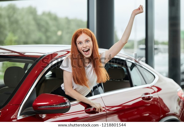 Car sale, consumerism and human emotions concept.\
Emotionally colored photo of overjoyed woman half sticking out from\
a car window screaming at camera, feeling herself the happiest\
woman at the world