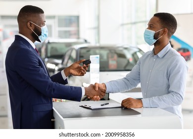 Car Sales. Black Salesman In Medical Mask Giving Key To Customer In Dealership Center, African American Man Buying New Vehicle During Coronavirus Pandemic, Handshaking With Salesperson After Deal