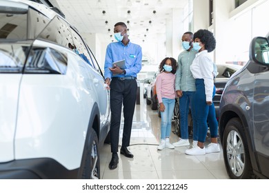 Car Sales Business During Covid-19 Quarantine. Manager Talking To Afro Family In Face Masks, Selling Auto At Dealership Shop. Young Black Clients Choosing New Vehicle At Automobile Showroom