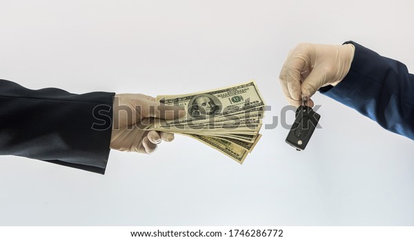 car sales\
in quarantine conditions coronavirus hands holding car key  and\
dollar bills isolated. Buying car\
concept