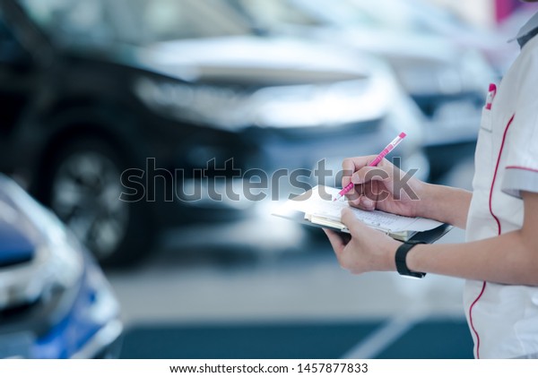 Car sales staff are writing car records in\
stock in the sales representative showroom., Taking notes on new\
cars in stock., Taking\
notes