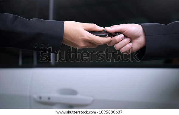 A car salesman or dealer is delivering car keys to\
customers in the showroom. Close-up of a hand holding a remote\
control. Having copy space.