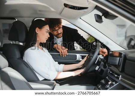 Car salesman explaining dashboard features to businesswoman sitting in driver's seat of a new car at the dealership