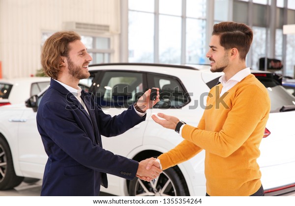 Car salesman giving key to customer while\
shaking hands in dealership
