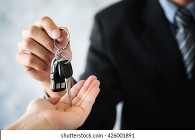 Car salesman giving the key to the new car owner transportation and ownership concept.