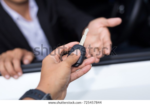 Car salesman handing over the\
key for a new car to a young businessman in front of the white\
car