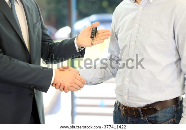 Car salesman handing over the keys for a new car to a\
young businessman . Handshake between two business people. Focus on\
a key