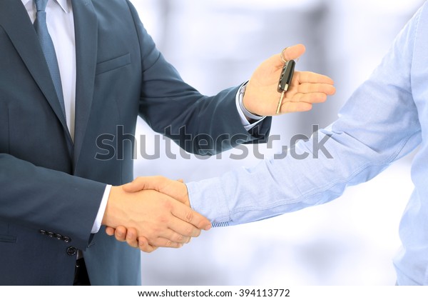 Car salesman handing over the keys for a new car to a\
young businessman . Handshake between two business people. Focus on\
a key