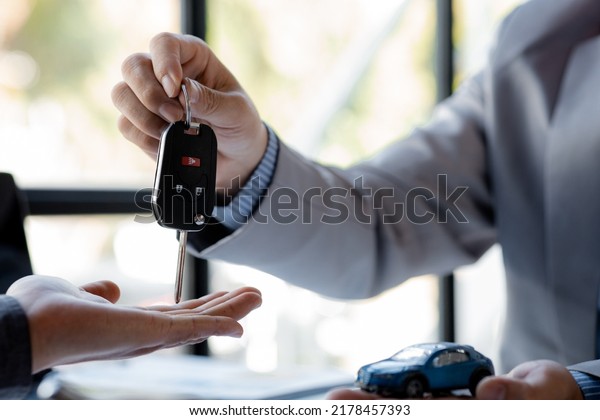 The car salesman hands the key to the customer\
after discussing the details and signing the purchase agreement,\
selling the car, selling the car from a major dealer. Vehicle sales\
concept.