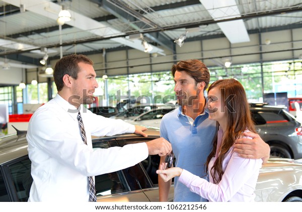 car salesman hands over the car key in the car\
dealership to customers