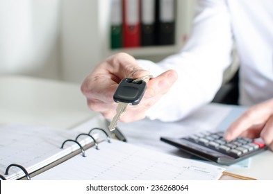 Car Salesman Holding A Key And Calculating A Price At The Dealership Office