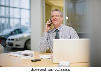 Car Salesman On Phone In Showroom