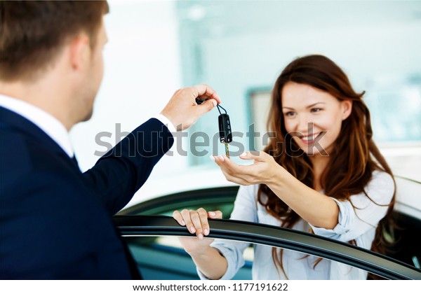 Car salesman sells a car to happy customer
in car dealership and hands over the
keys
