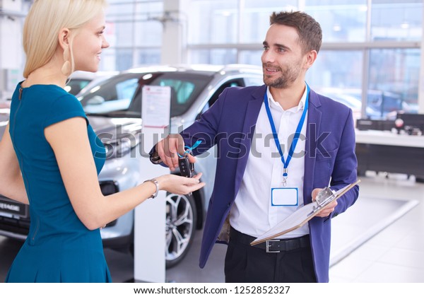 Car salesman sells a car to happy customer\
in car dealership and hands over the\
keys