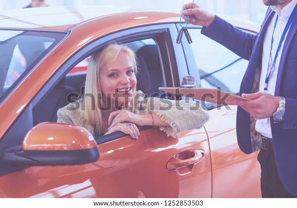 Car salesman sells a car to happy customer\
in car dealership and hands over the\
keys