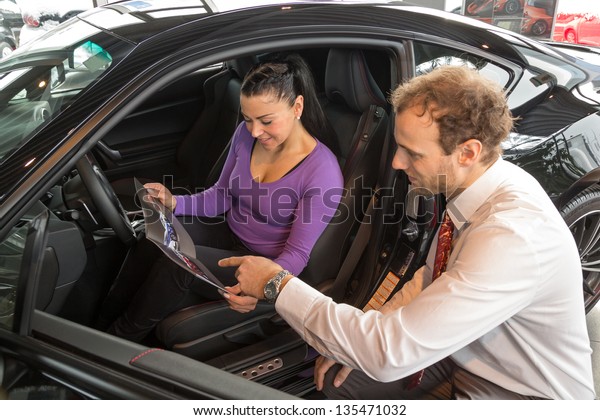 Car salesman sells a car to happy customer\
in car dealership and hands over the\
keys.