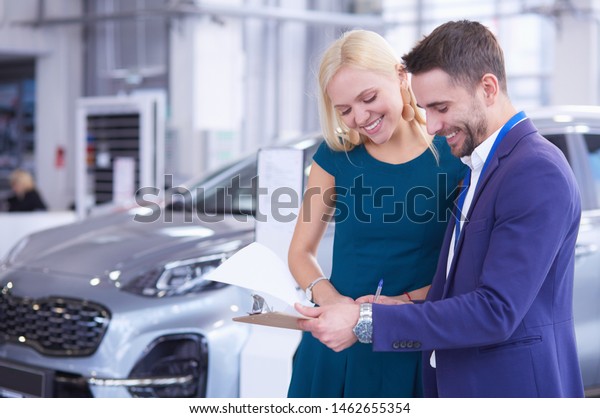 Car salesman sells a car to happy customer\
in car dealership and hands over the\
keys.