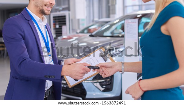 Car salesman sells a car to happy customer
in car dealership and hands over the
keys