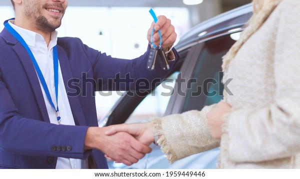 Car salesman sells a car to happy customer
in car dealership and hands over the
keys.