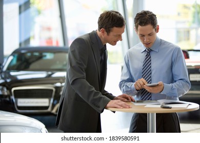 Car Salesman Showing Cost Calculation To A Customer On His Phone With Documents Are Lying On The Table Along With The Car Keys.