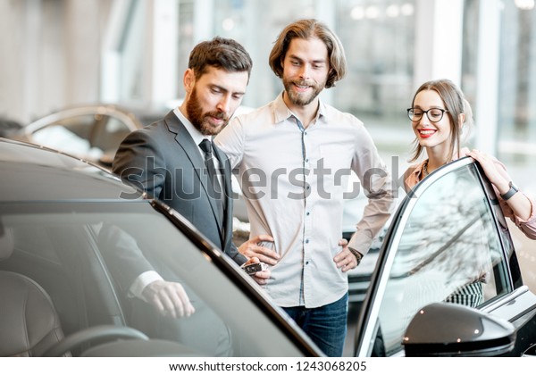 Car salesman showing car interior to a young
couple clients in the
showroom