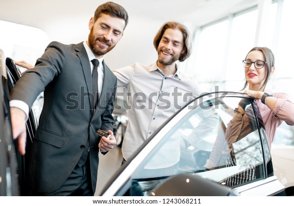 Car salesman showing car interior to a young\
couple clients in the\
showroom
