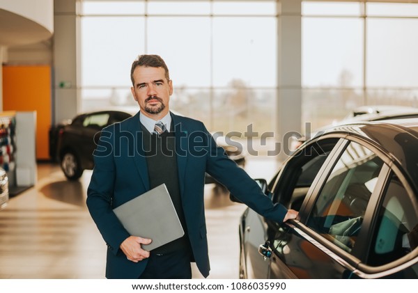 Car salesman\
standing beside a car at\
showroom.