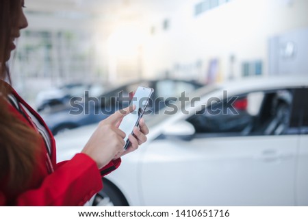 Car salesmen, beautiful women, Asian women holding smartphones, touching the phone screen to check new car stock in car showrooms, automotive businesses, car sales, management, gestures and people.