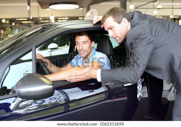 car salesmen and customers\
talk about the technology of a car in the showroom of a car\
dealership 