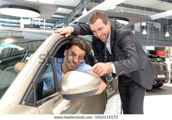 car salesmen and customers\
talk about the technology of a car in the showroom of a car\
dealership 