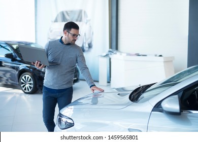 Car Salesperson With Laptop Checking Vehicle Specifications In Local Dealership Showroom. Vehicle Dealership.