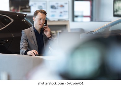 Car Salesperson Talking On Landline Phone While Working In Showroom