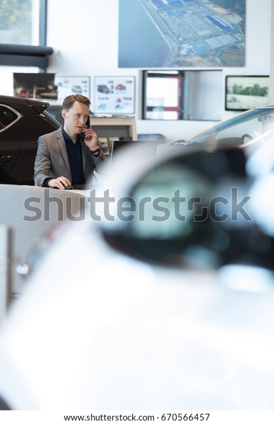 Car salesperson talking on landline phone while\
working in car showroom