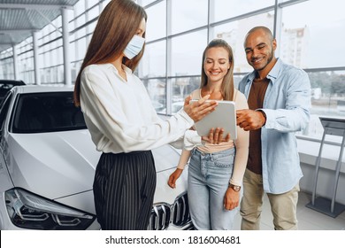 Car Saleswoman Wearing Medical Mask Shows Buyers Couple Something On Digital Tablet