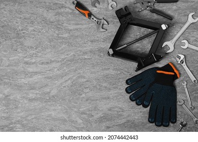 Car scissor jack, gloves and different tools on grey stone surface, flat lay. Space for text